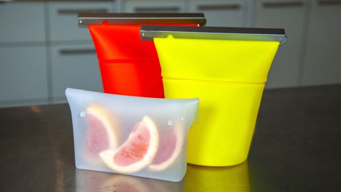 Three reusable silicone bags, one is red, one is neon yellow, and one is see-through with grapefruit