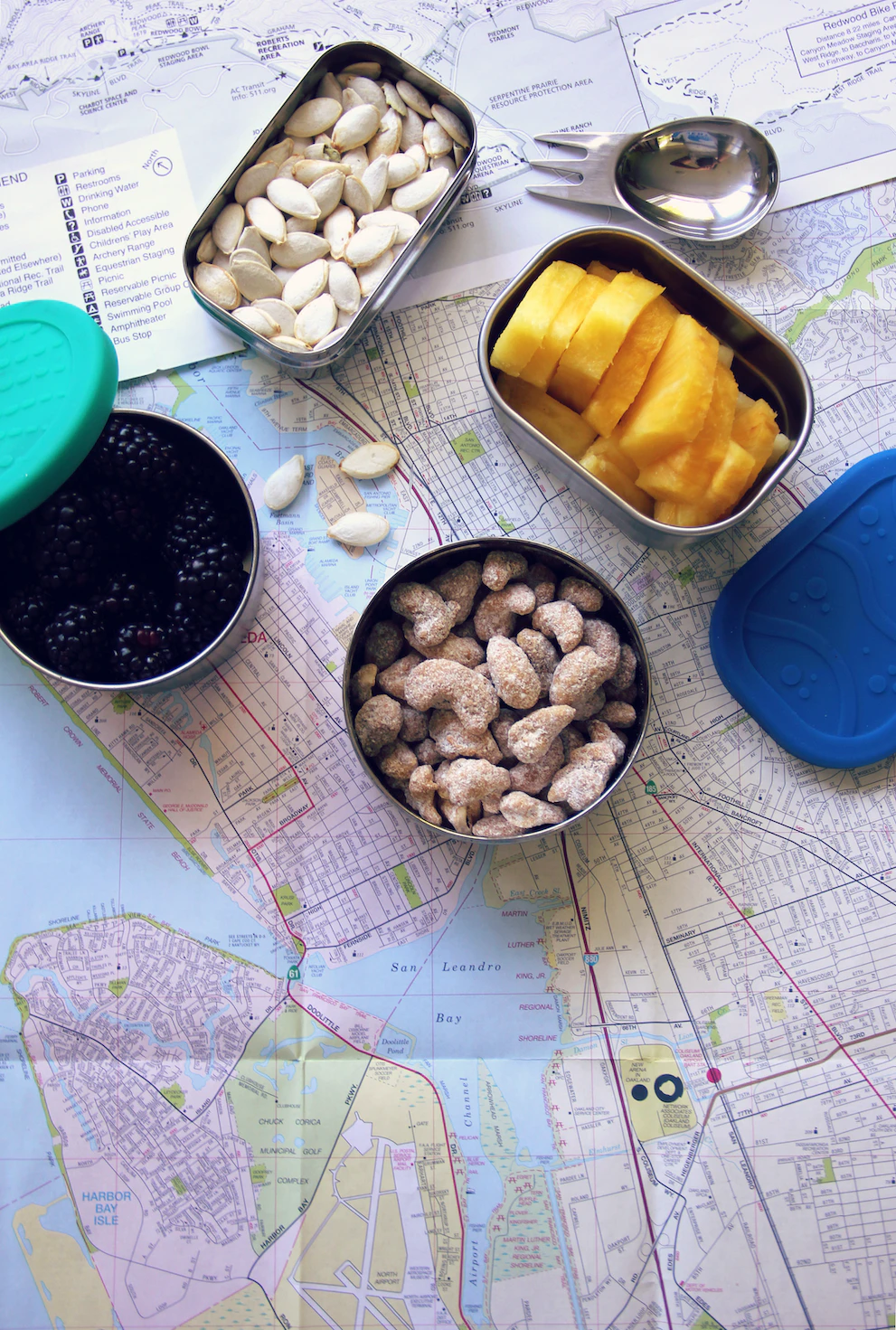 several stainless steel food containers are rested on top of a map, filled with snack including fruit and nuts