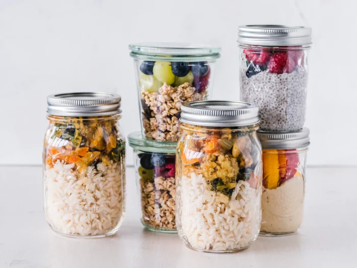 Six mason jars arranged on a neutral background displaying various meals inside