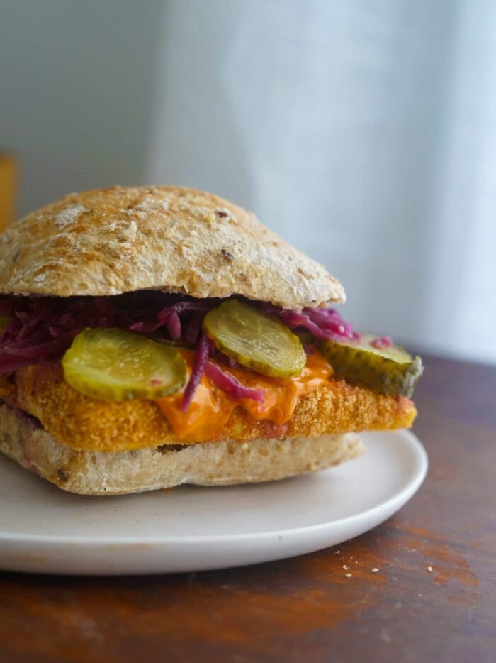 Dill Pickle Tofu Sandwich served with pickles, sriracha mayo, and red cabbage.