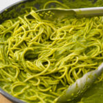 a big pan of spaghetti with a bright green sauce