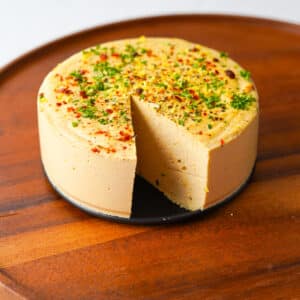 a round block of vegan hard cheese with a slice out of it on a cutting board