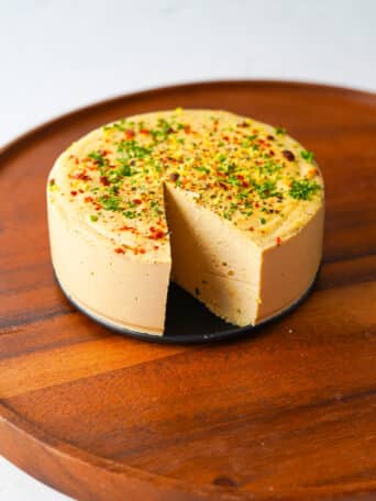 a round block of vegan hard cheese with a slice out of it on a cutting board