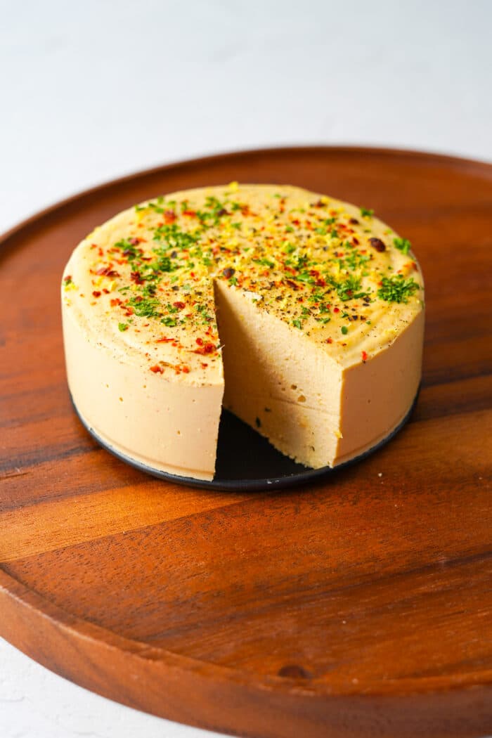 a round block of vegan hard cheese with a slice out of it on a cutting board