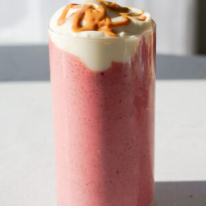 pink smoothie on white backdrop with yogurt and peanut butter drizzled over top