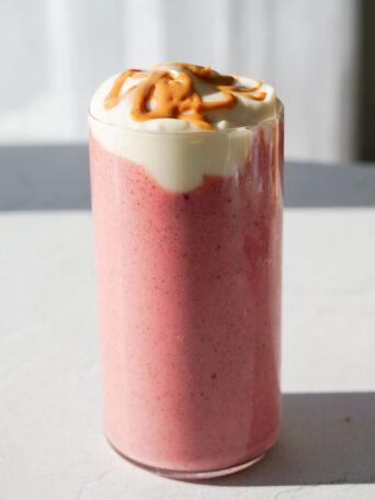 pink smoothie on white backdrop with yogurt and peanut butter drizzled over top