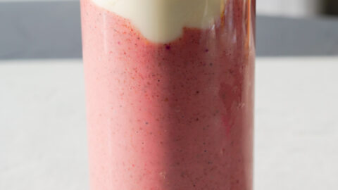 pink smoothie on white backdrop with yogurt and peanut butter drizzled over top