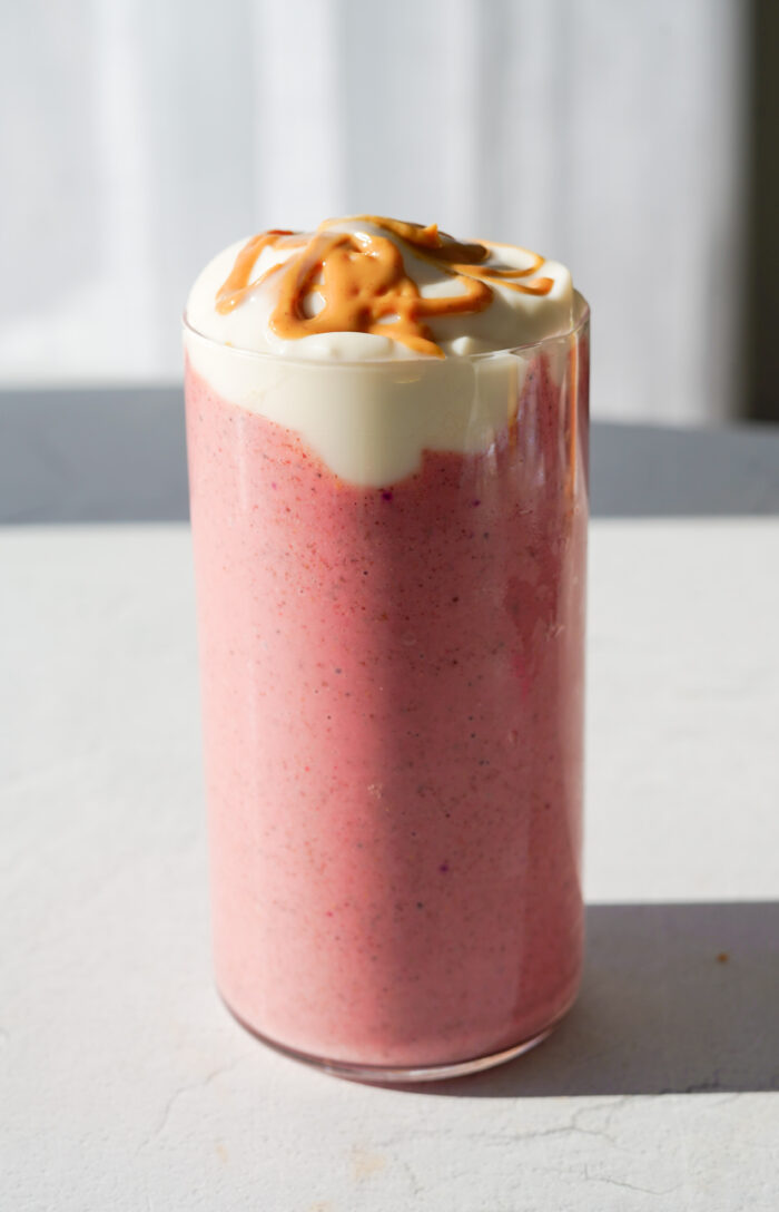 pink smoothie on white backdrop with yogurt and peanut butter drizzled over top