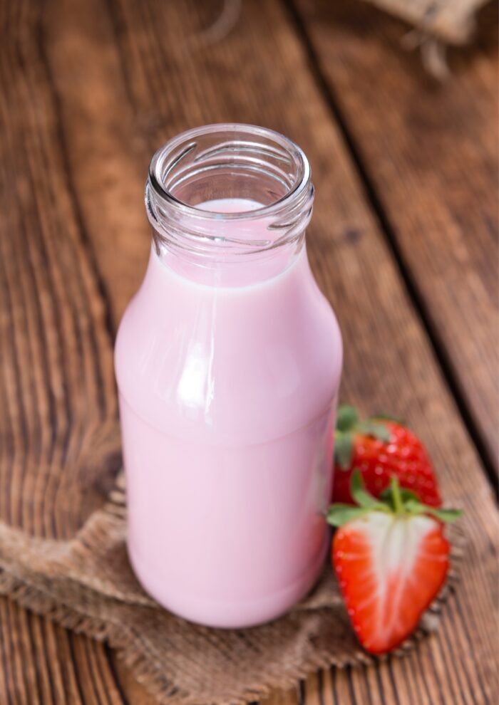 a clean jar of strawberry milk with strawberries laying next to it