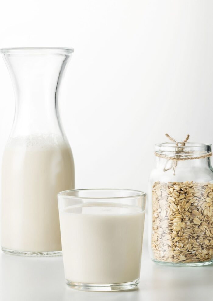 2 jars of oat milk sitting on a grey counter with a jar of oats to the right side