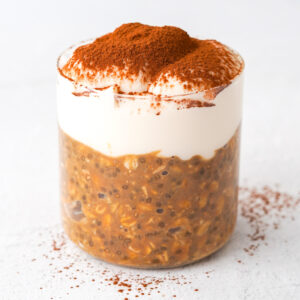 overnight oats with yogurt and cocoa powder sprinkled over top sitting on a white table