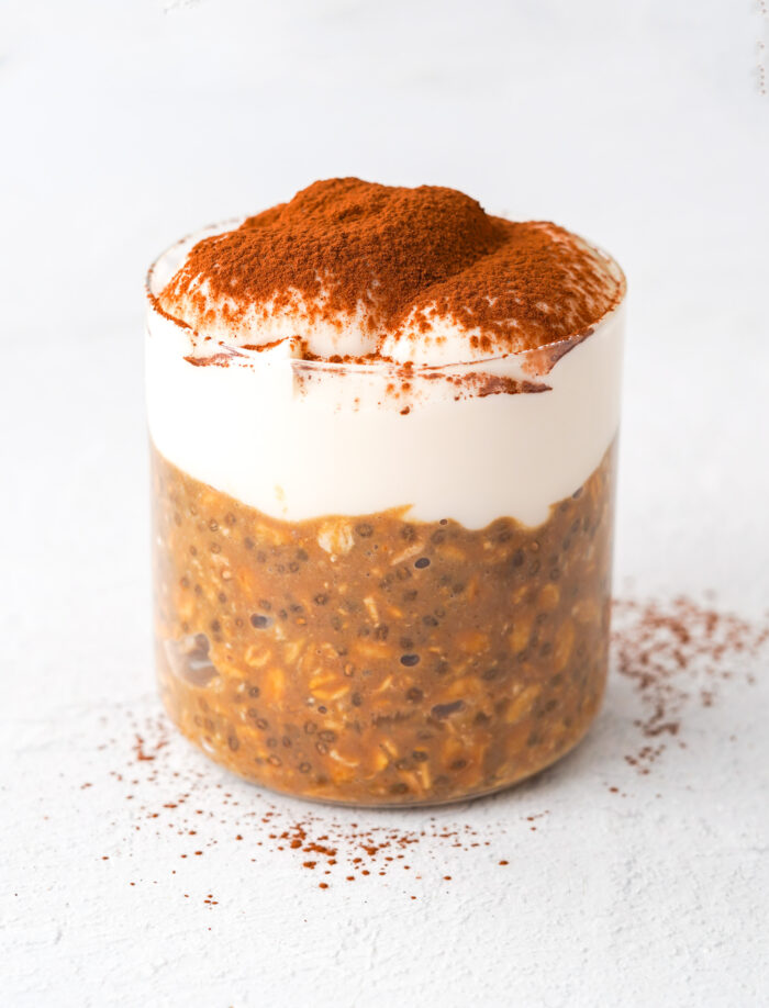 overnight oats with yogurt and cocoa powder sprinkled over top sitting on a white table