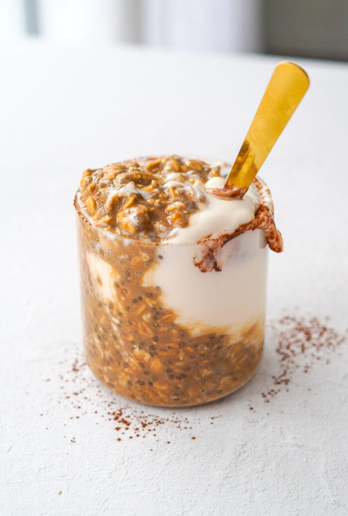 mixed chocolate and coffee overnight oats with a gold spoon sitting on a white table