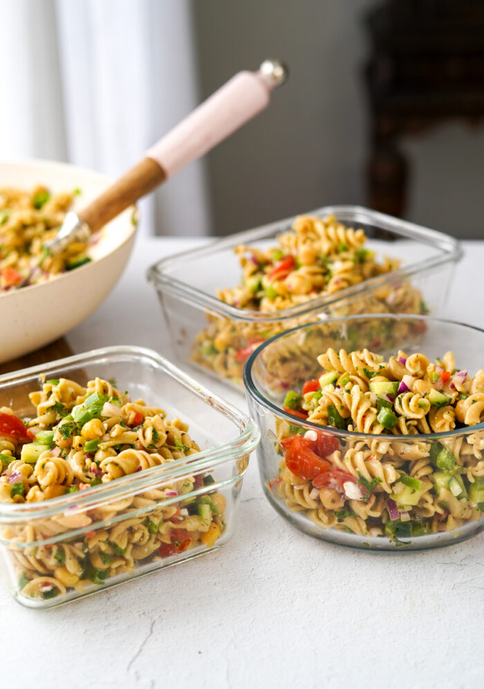 vegan greek pasta salad separated into clear glass storage containers for meal prep