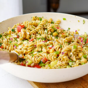 vegan greek pasta salad mixed together in a large white mixing bowl on top of a wooden cutting board