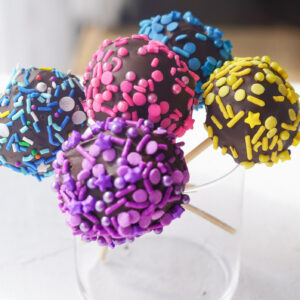 cake pops with multicoloured sprinkles sitting in a glass jar