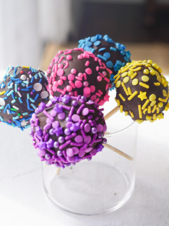 cake pops with multicoloured sprinkles sitting in a glass jar