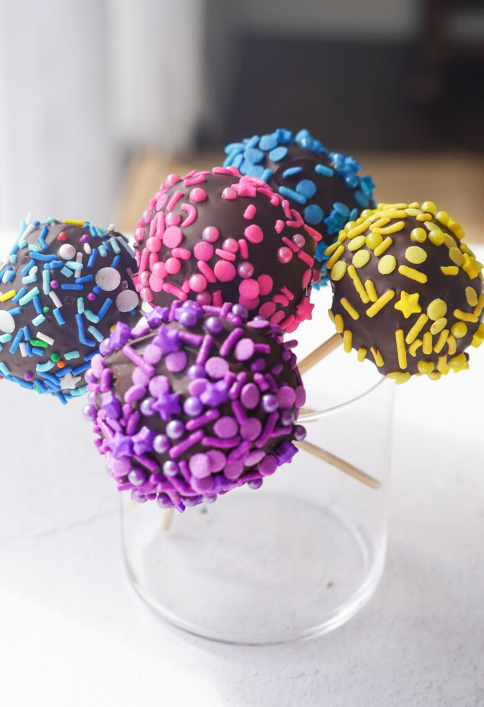 cake pops with multicoloured sprinkles sitting in a glass jar