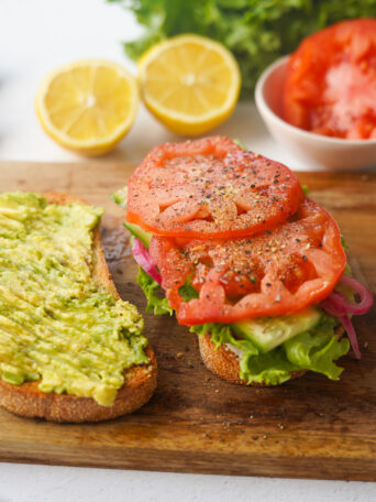 an open faced sandwich on a cutting board with avocado on one side and tomatoes on the other with salt, pepper and garlic seasoning