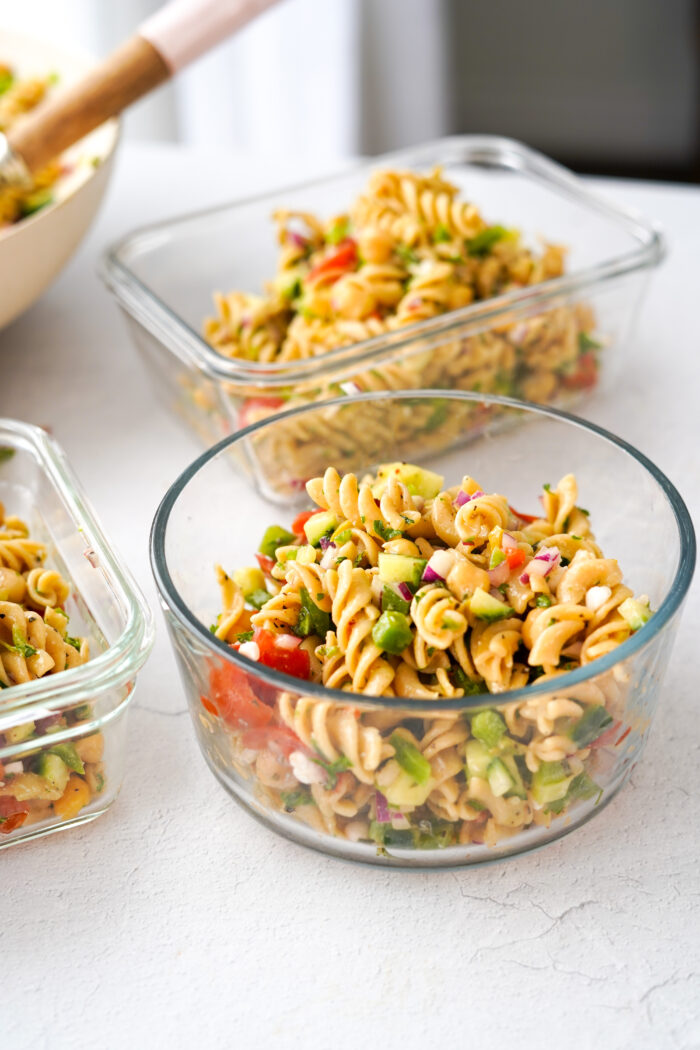 vegan greek pasta salad separated into clear glass storage containers for meal prep