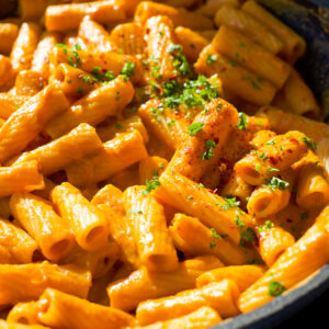rigatoni noodles covered in a rose sauce in a skillet with parsley sprinkled on top