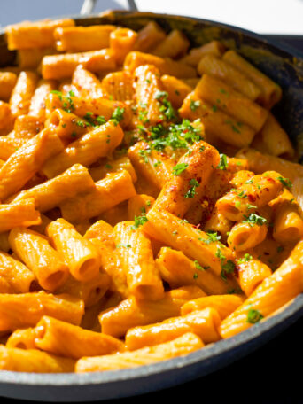 rigatoni noodles covered in a rose sauce in a skillet with parsley sprinkled on top