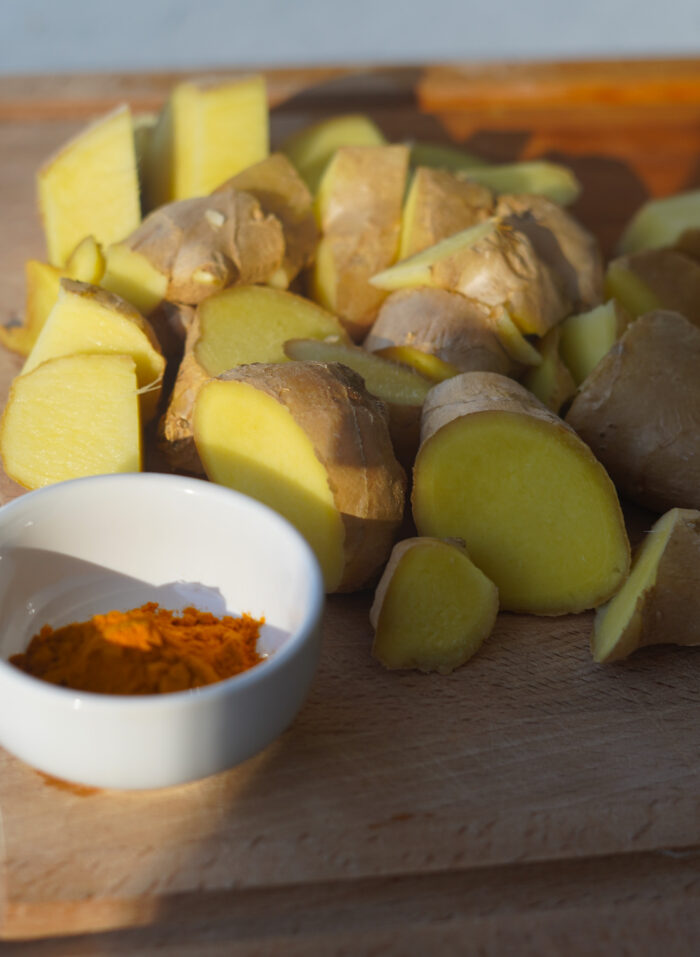 chopped up ginger root set on a wooden chopping board with a small dish of turmeric