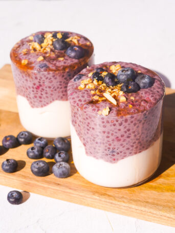 two blueberry chia pudding cups on a wood cutting board with granola and blueberries on top