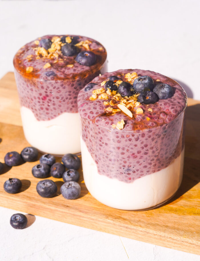 two blueberry chia pudding cups on a wood cutting board with granola and blueberries on top