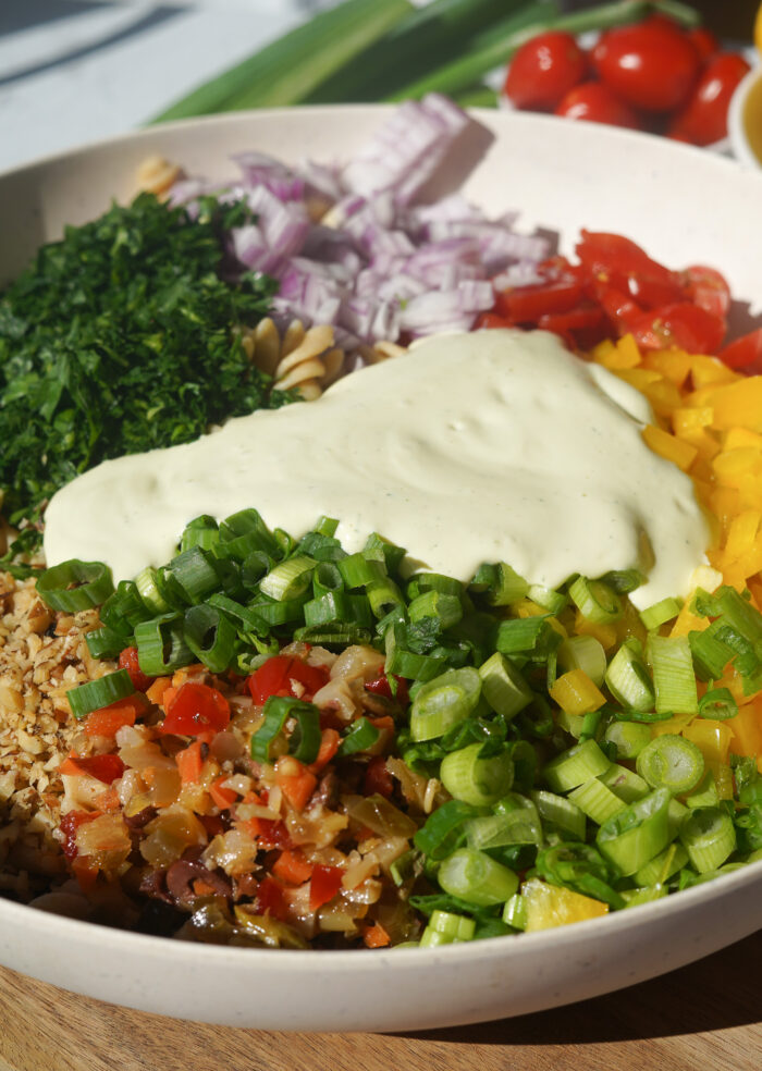 a colourful pasta salad with green onion, bell pepper, tomato and dill in a big white bowl