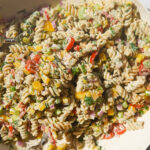 a white bowl full of a creamy rotini pasta salad with vegetables