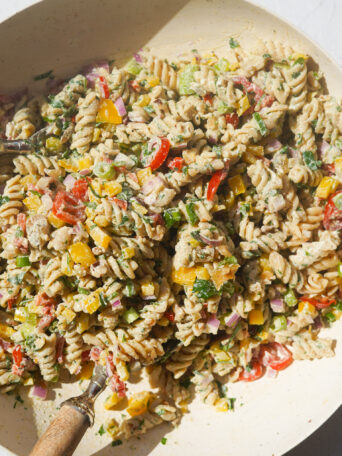 a white bowl full of a creamy rotini pasta salad with vegetables