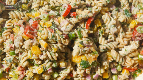 a white bowl full of a creamy rotini pasta salad with vegetables