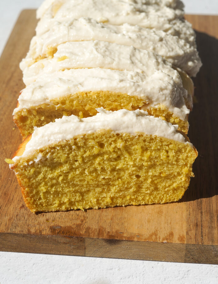 vegan lemon loaf with vanilla frosting sliced on a wooden cutting board