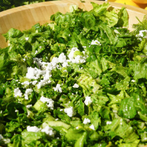 cucumber, parsley, dill, vegan feta, green onions and lettuce sitting in a wooden bowl on a white counter