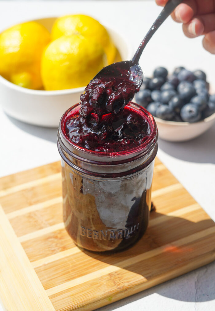 blueberry jam sitting in a small jar on a wood cutting board with a spoon in it