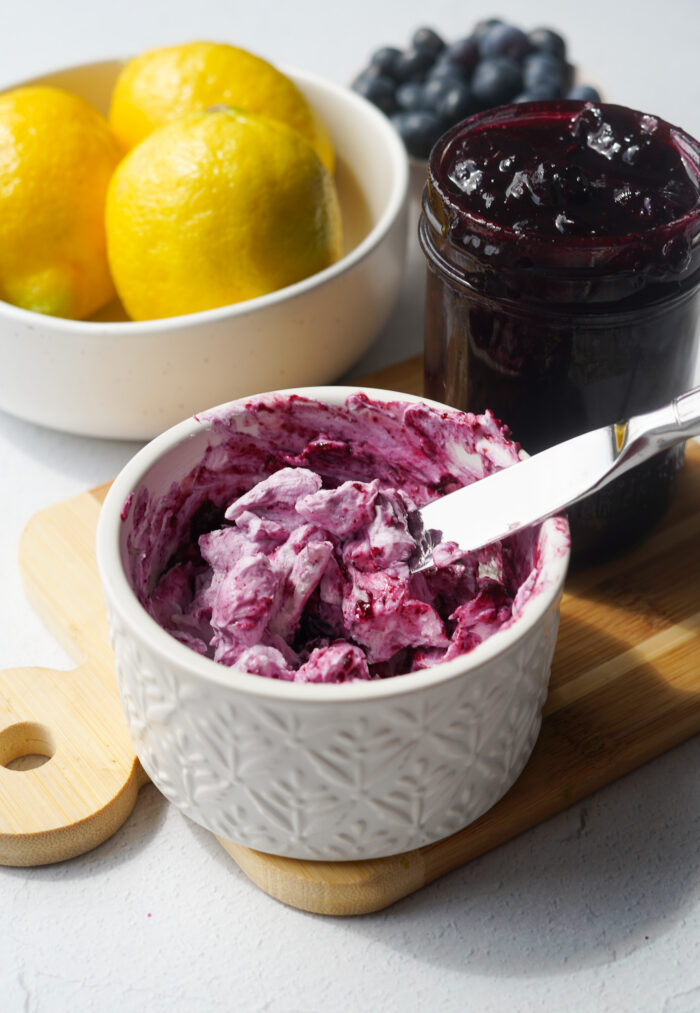 blueberry jam mixed with vegan cream cheese sitting in a white container on a wood cutting board