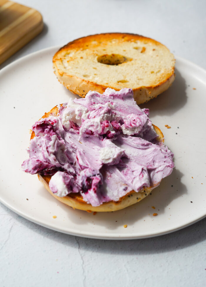 an open faced bagel with vegan cream cheese swirled with blueberry jam