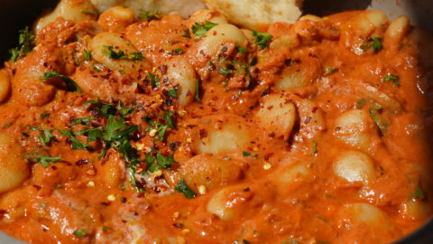 a grey pan full of butter beans in a red sauce with a naan at the back