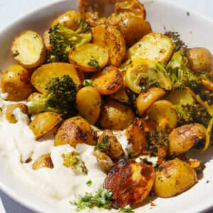 mini potatoes, baked lemon and baked broccoli in a bowl with vegan whipped feta dip on a white backdrop