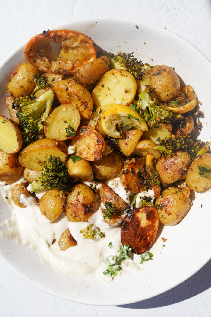 mini potatoes, baked lemon and baked broccoli in a bowl with vegan whipped feta dip on a white backdrop