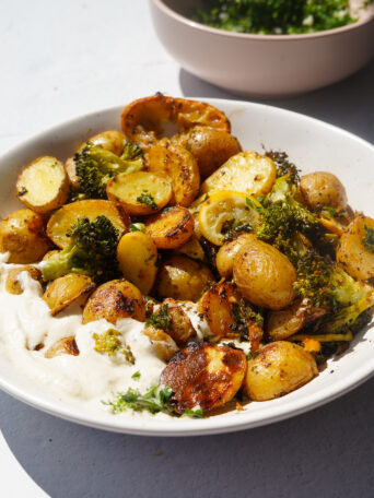 mini potatoes, baked lemon and baked broccoli in a bowl with vegan whipped feta dip on a white backdrop