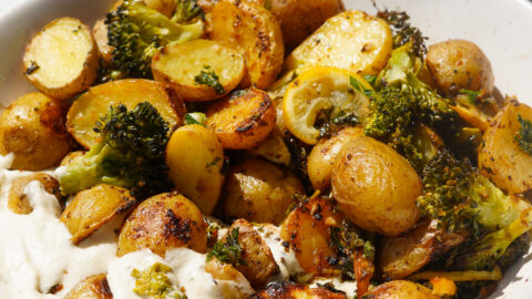 mini potatoes, baked lemon and baked broccoli in a bowl with vegan whipped feta dip on a white backdrop