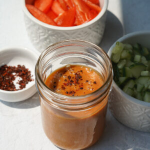 peanut sauce sitting in a jar surrounded by a small bowl with peppers and cucumbers