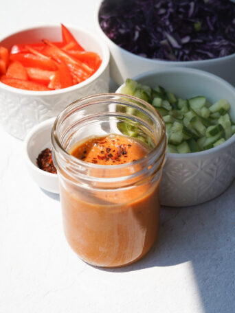 peanut sauce sitting in a jar surrounded by a small bowl with peppers and cucumbers