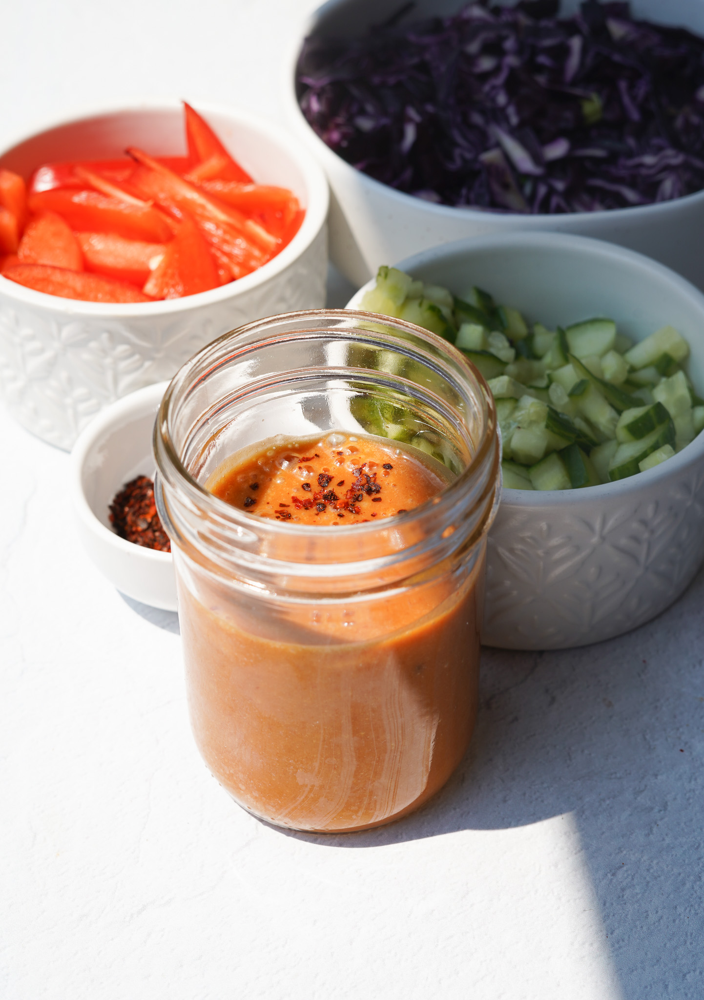 peanut sauce sitting in a jar surrounded by a small bowl with peppers and cucumbers