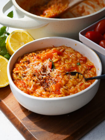 tomato orzo served in a white bowl with ingredients and pot behind