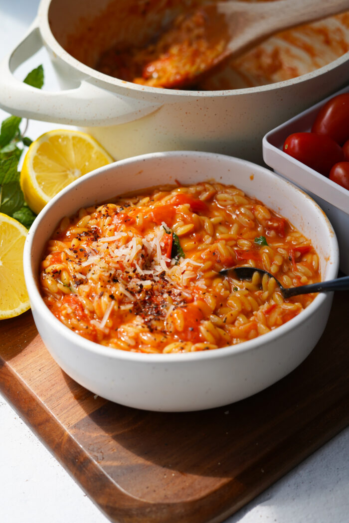 tomato orzo served in a white bowl with ingredients and pot behind
