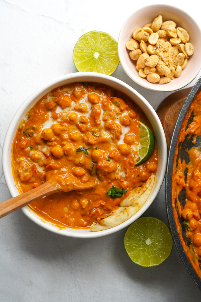 peanut butter curry served in a white bowl with a wedge of lime and naan, top down view