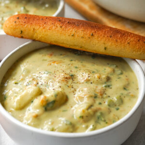 vegan Olive Garden gnocchi soup presented in a white bowl with a breadstick rested across and more soup in the background